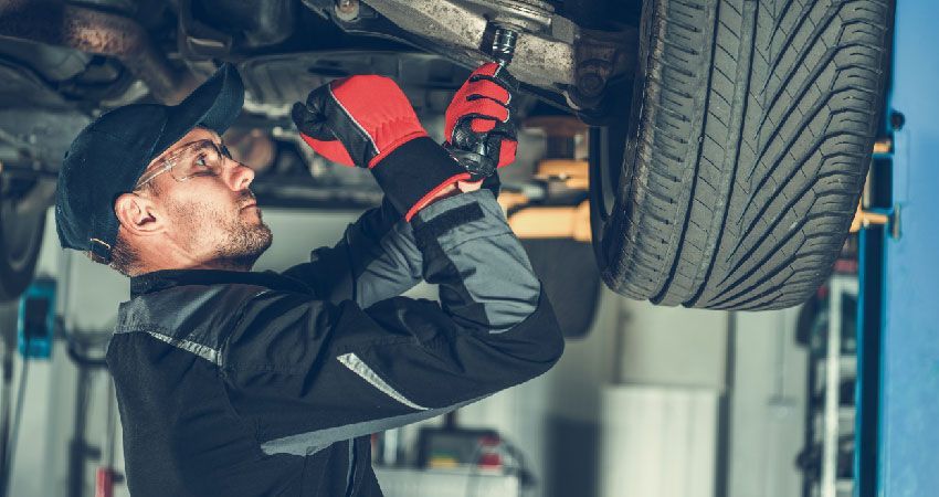 Mechanic with red gloves on underneath a car inspecting the left side of the vehicles suspension