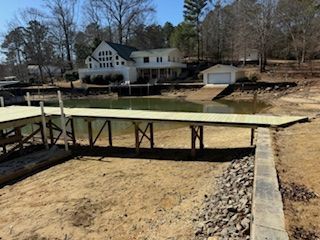 A dock with a house in the background is next to a body of water.