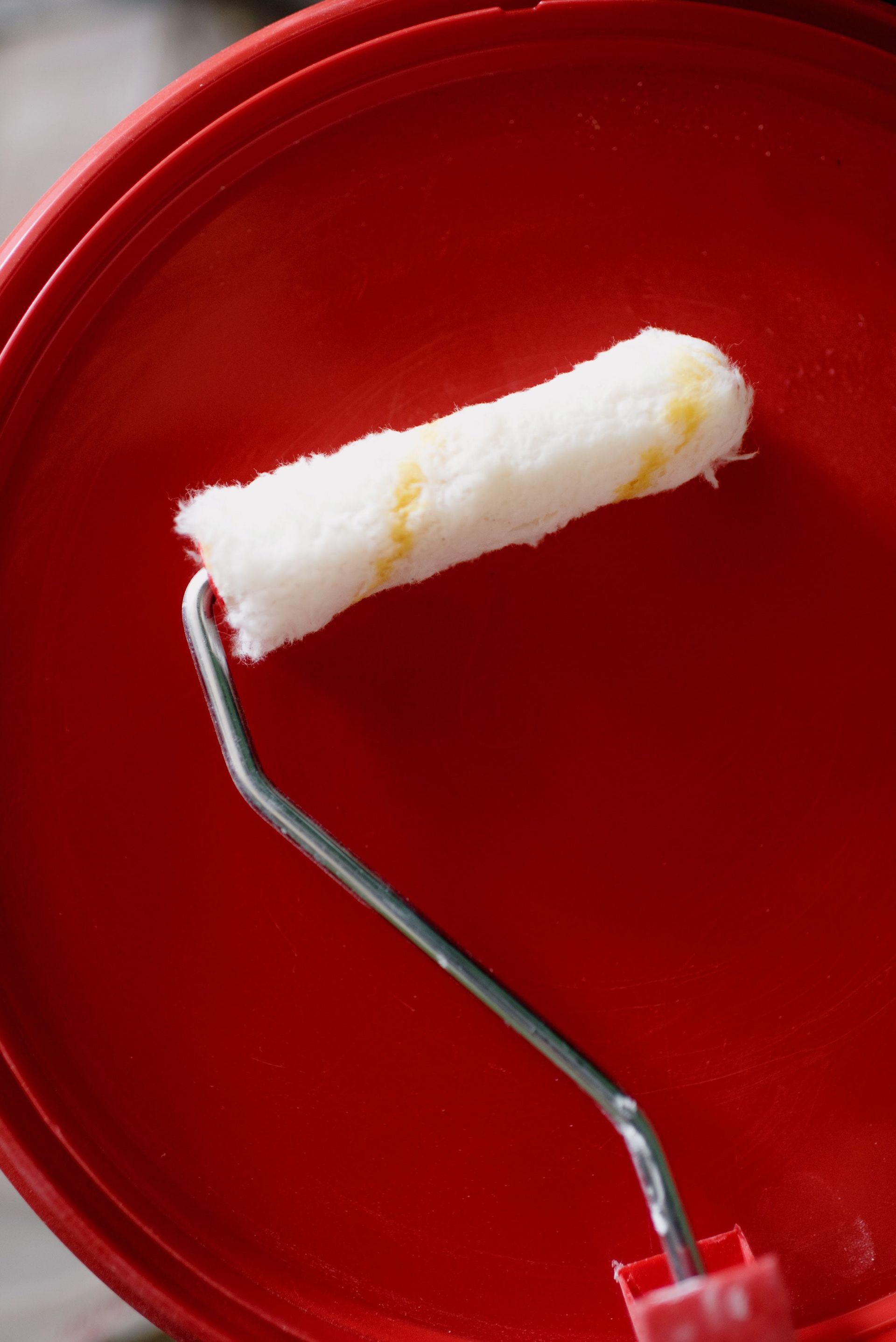 A paint roller is sitting on top of a red bucket