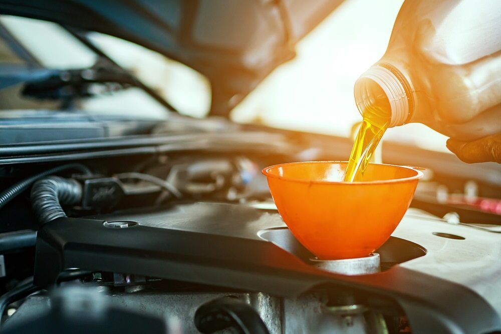 A Person Is Pouring Oil Into A Cup Under The Hood Of A Car — Superior Machinery Maintenance In Ryan, QLD