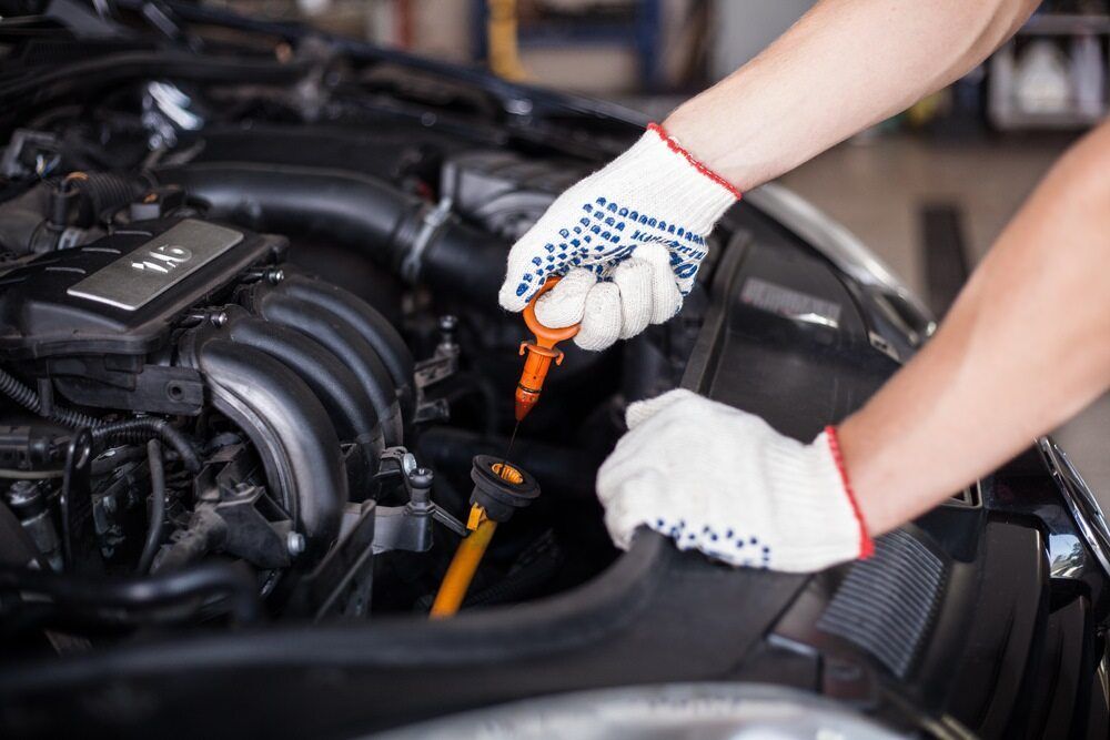 A Man Is Checking The Oil Level Of A Car Engine — Superior Machinery Maintenance In Ryan, QLD