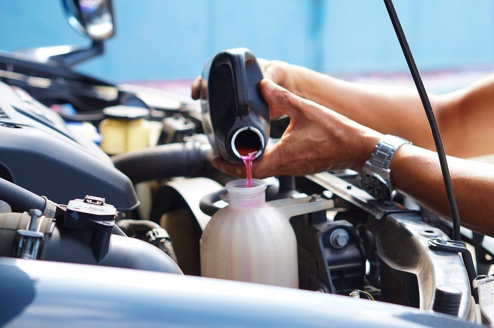 A Person Is Pouring Coolant Into A Bottle In A Car — Superior Machinery Maintenance In Ryan, QLD