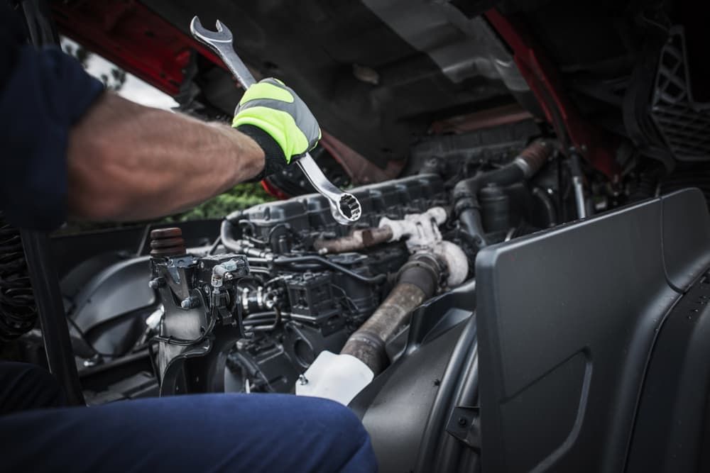 A Man Is Working On A Truck Engine With A Wrench — Superior Machinery Maintenance In Ryan, QLD