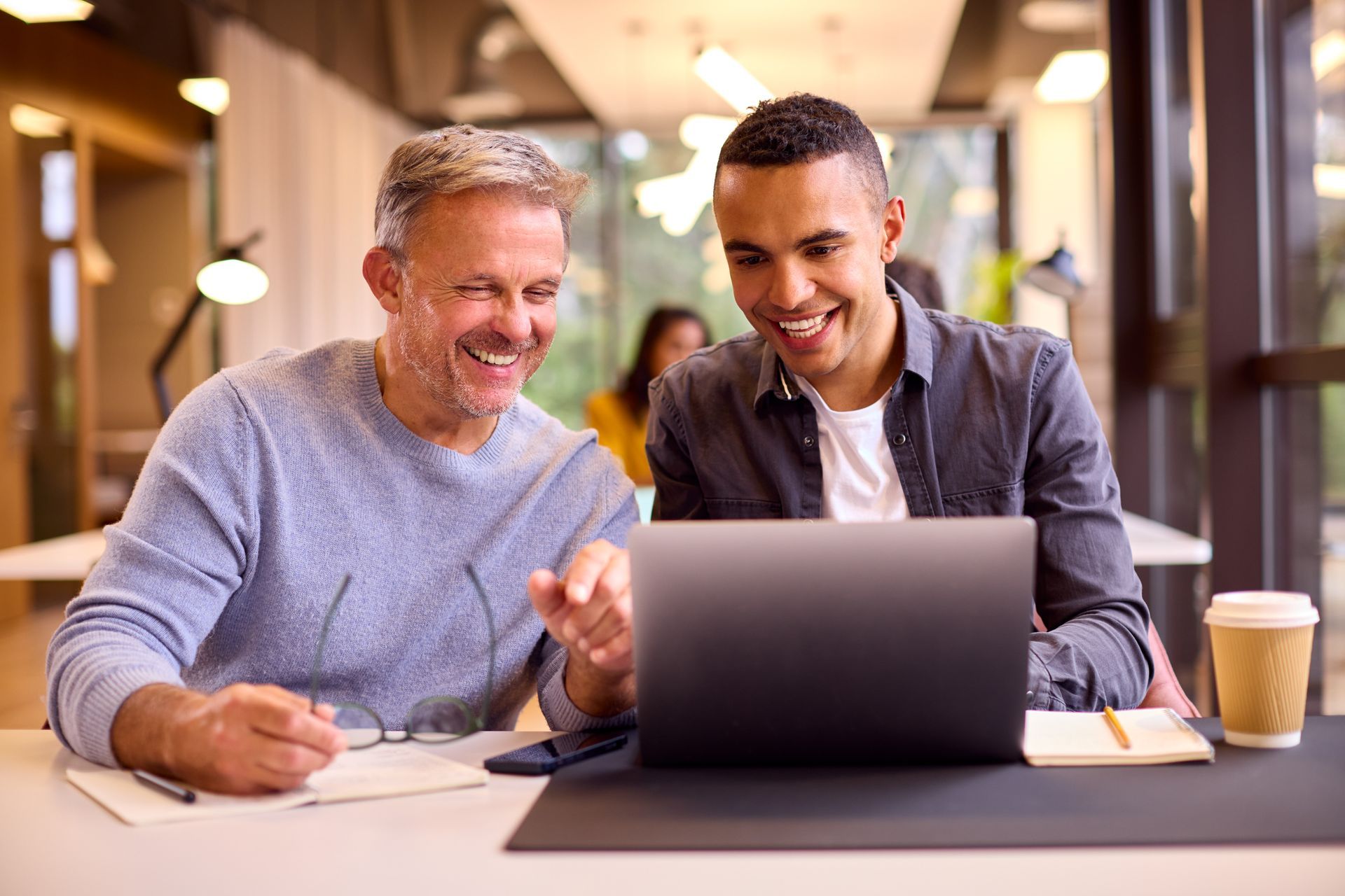 Two men are sitting at a table looking at a laptop computer.