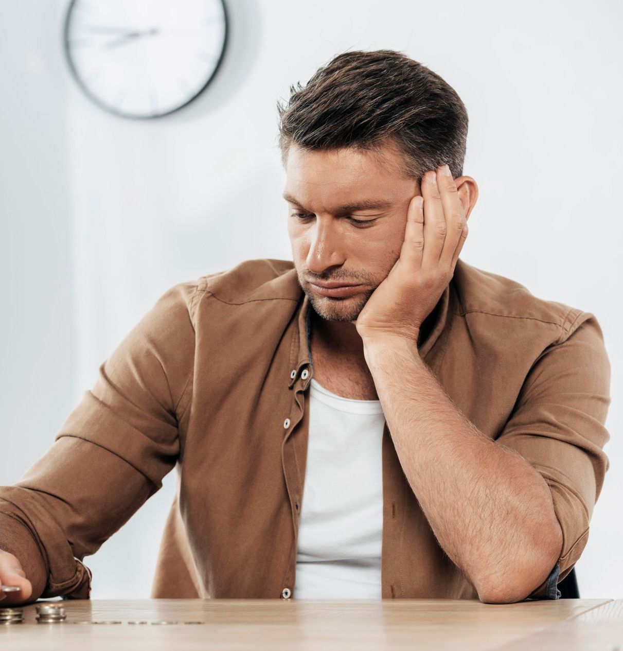 A man in a brown shirt is sitting at a table with his head resting on his hand.