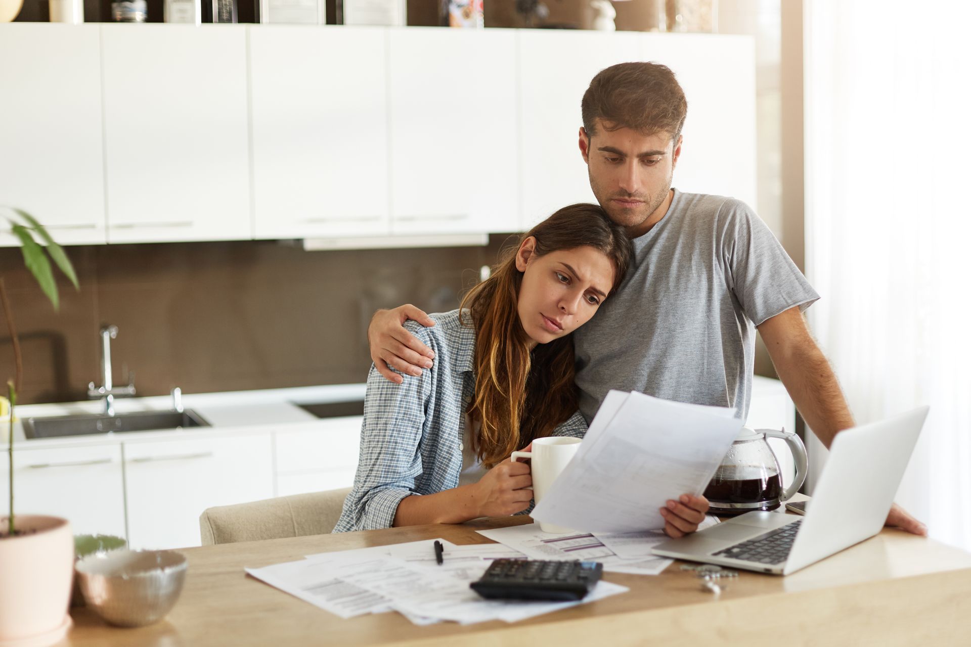 A man and a woman are sitting at a table looking at papers and a laptop.