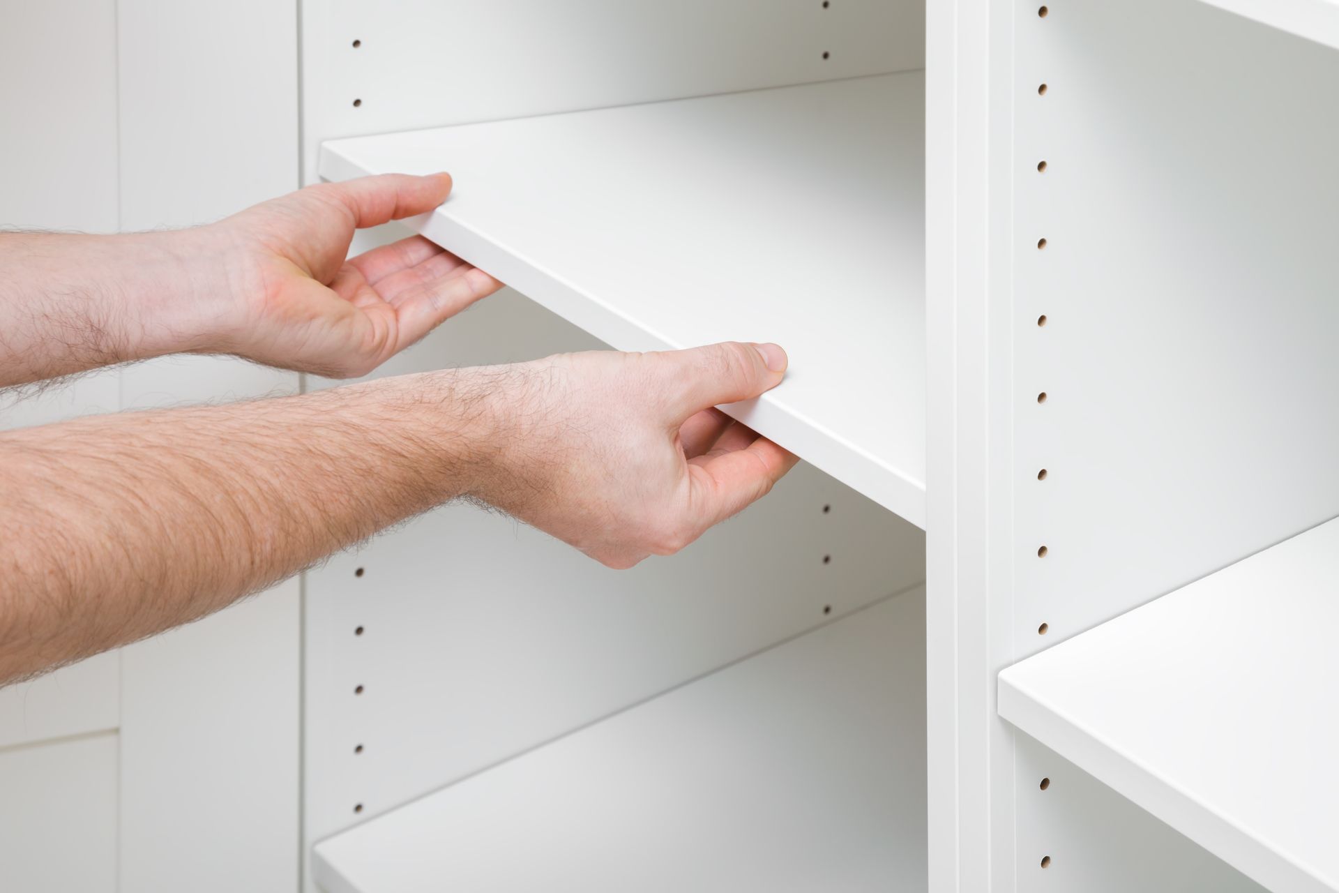 Hands installing a white shelf in a white shelving unit.