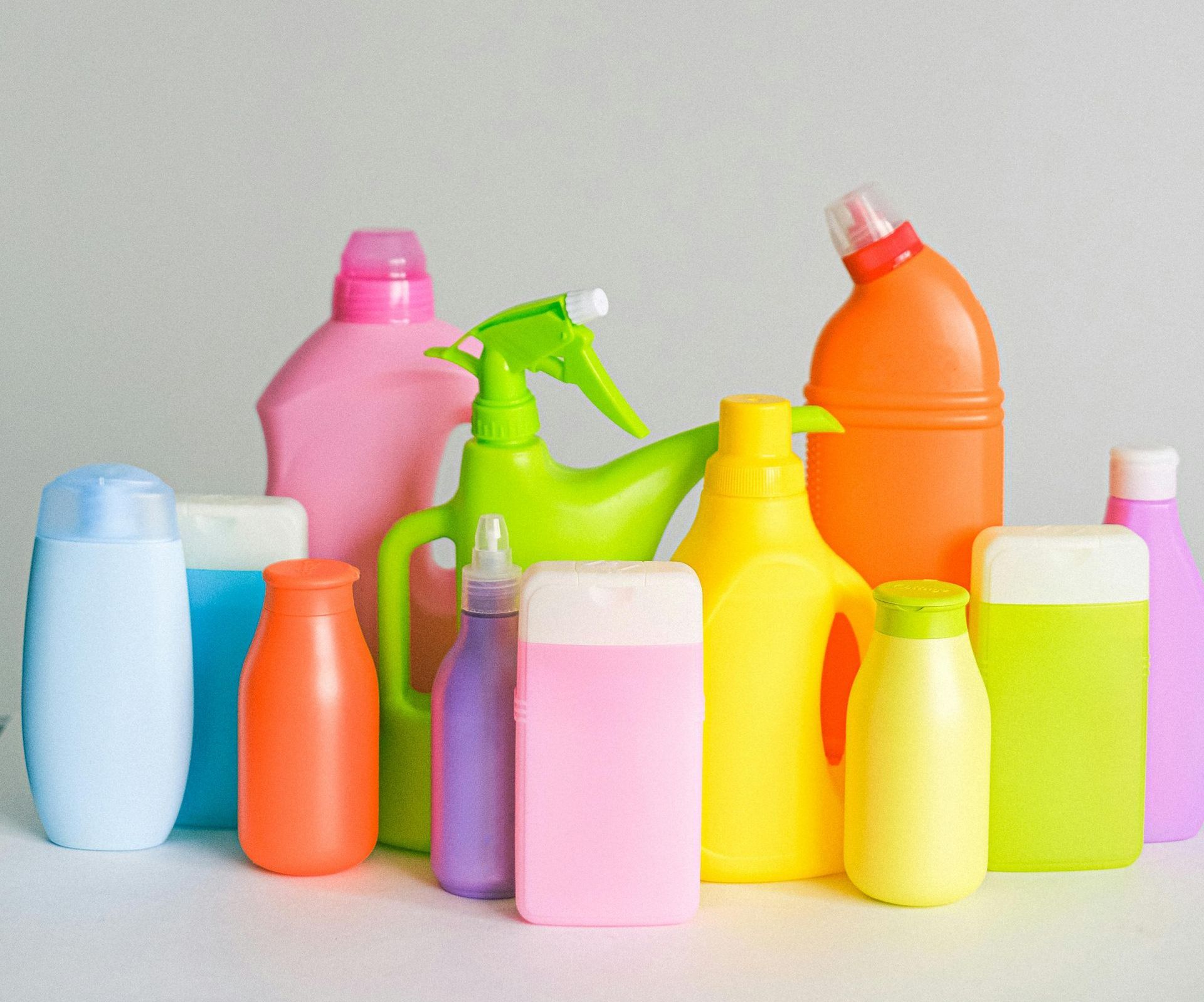 A bunch of colorful plastic bottles are lined up on a table with cleaning product
