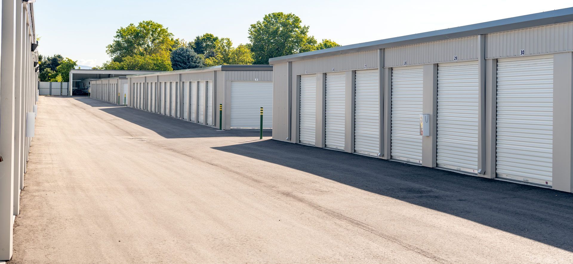 Exterior view of a self-storage facility, rows of individual units with white doors, gray walls, and an asphalt driveway.
