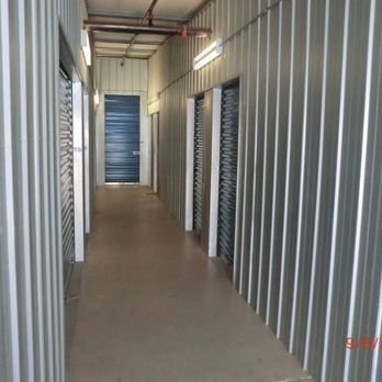 Interior of a storage unit facility corridor. Metal walls, multiple unit doors, and a blue door at the end.