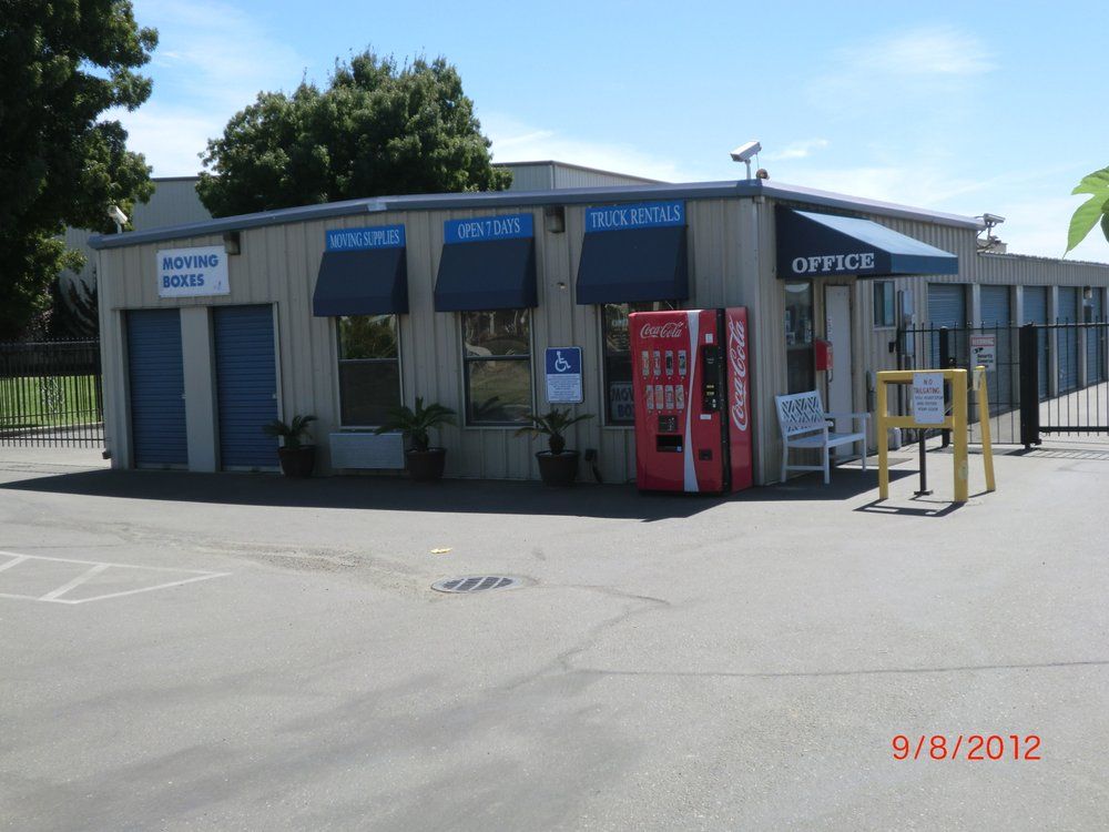 Storage facility office with blue awnings, a vending machine, and accessible parking sign.