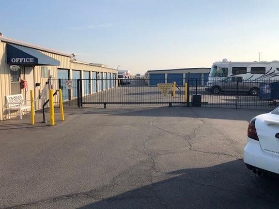 Storage facility with office, gate, storage units, and vehicles.