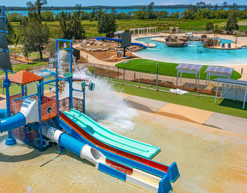 Aerial view of Yamba campground with cabins and RVs beside a waterway. Blue sky, water, and green trees.