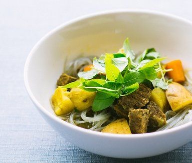 Bowl of beef stew with noodles, potatoes, carrots, and basil garnish.