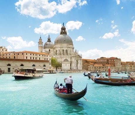 Venice canal with gondola, boats, and Basilica di Santa Maria della Salute under a blue sky.
