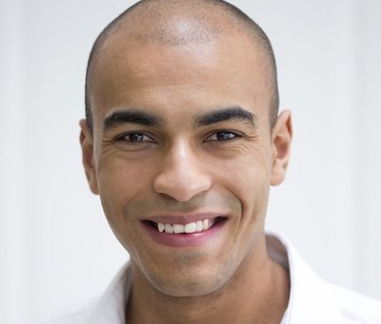 Smiling man with a shaved head. He is wearing a white shirt and looking directly at the camera.