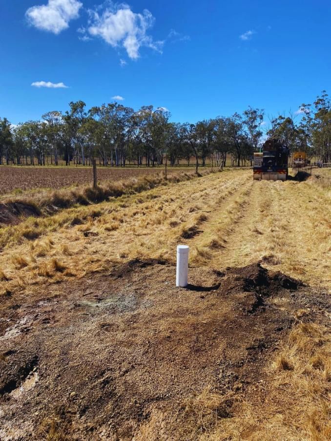 A Rural Field With a White Pipe, Dry Grass, and a Truck — Local Drilling Services In North Burnett, QLD