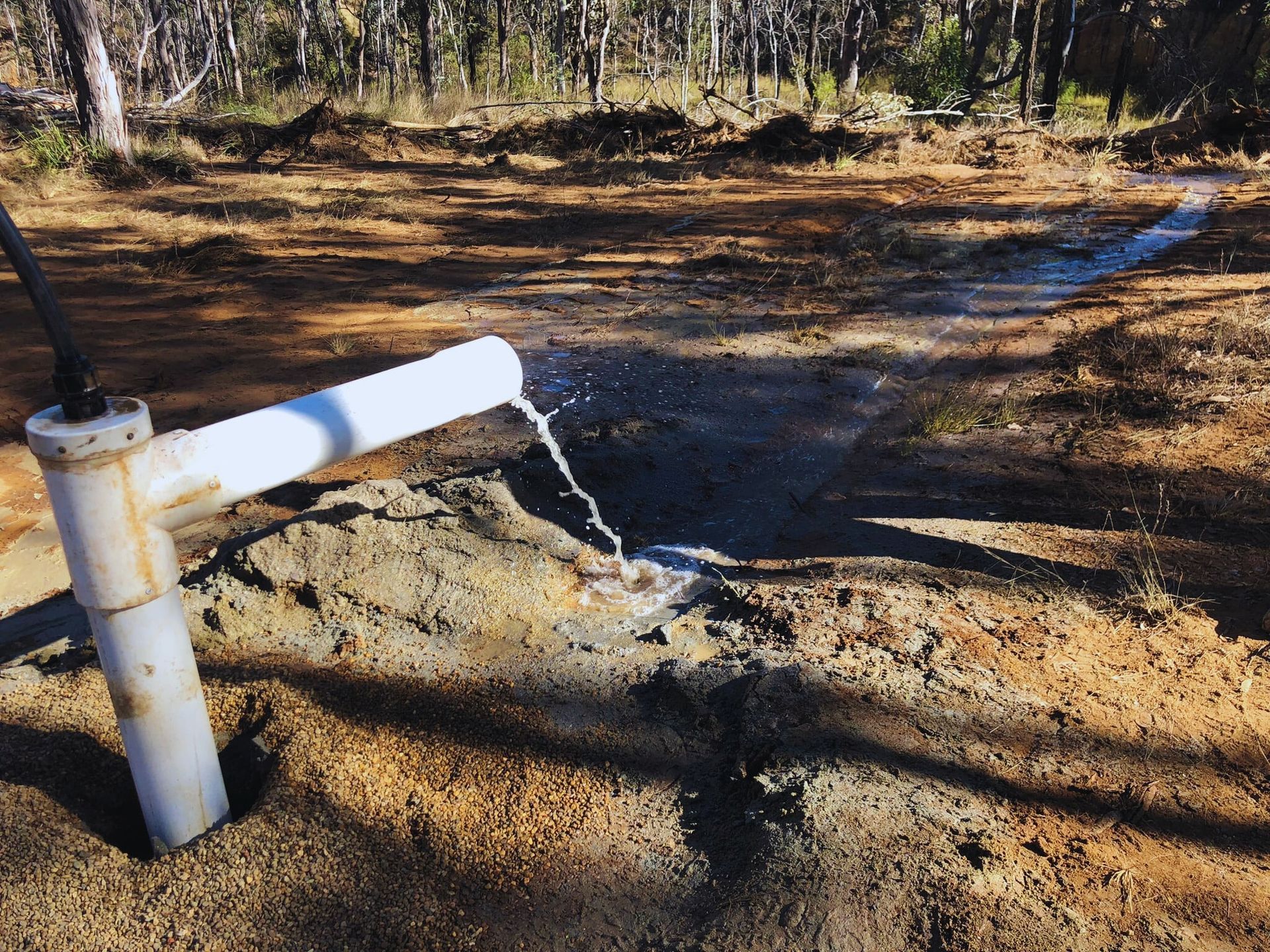 White pipe spews water into a trench dug in sandy soil, outdoors — Local Drilling Services In South Burnett, QLD