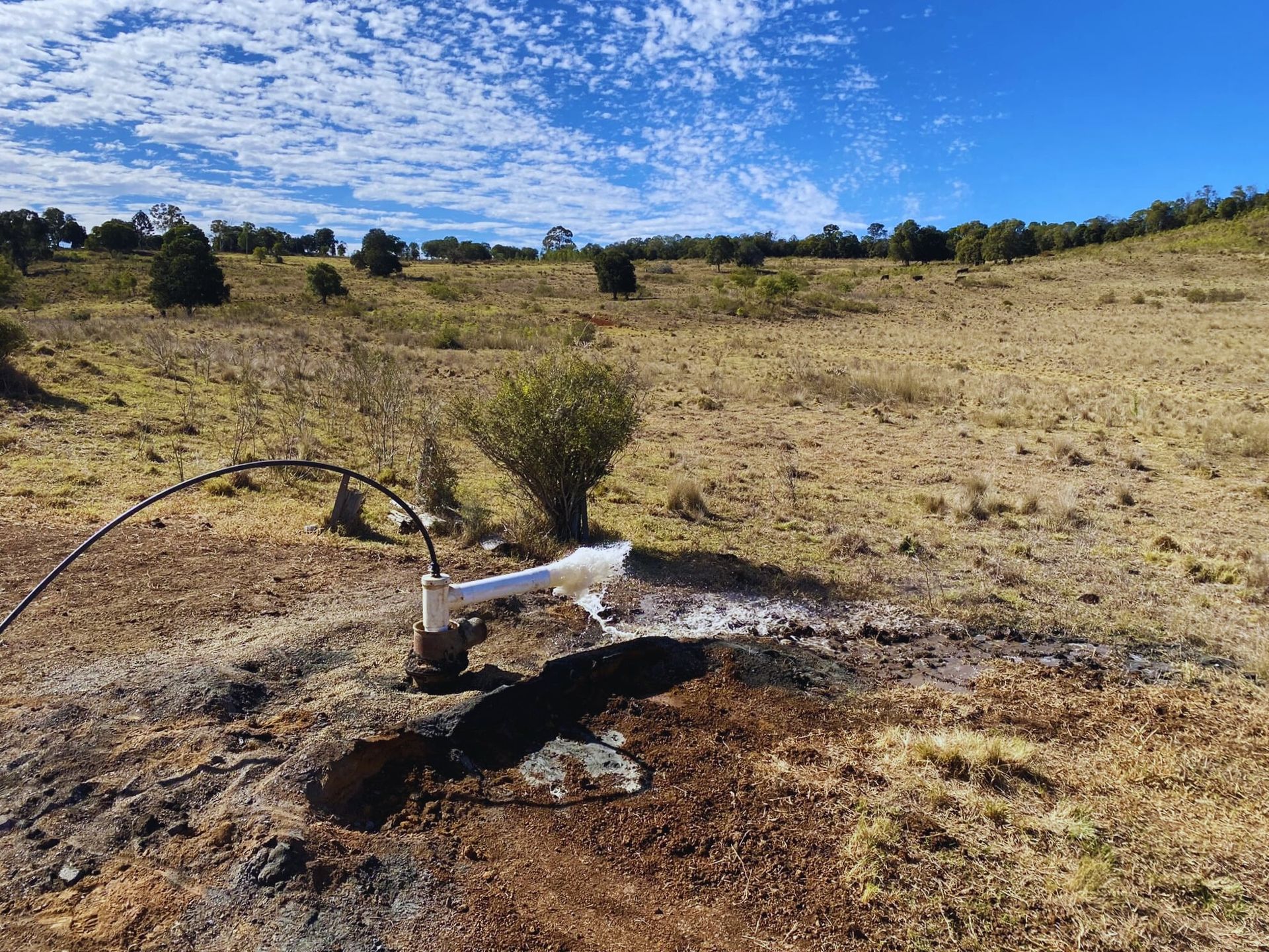 Water gushing from a well in a dry field under a bright blue sky with sparse clouds — Local Drilling Services In South Burnett, QLD