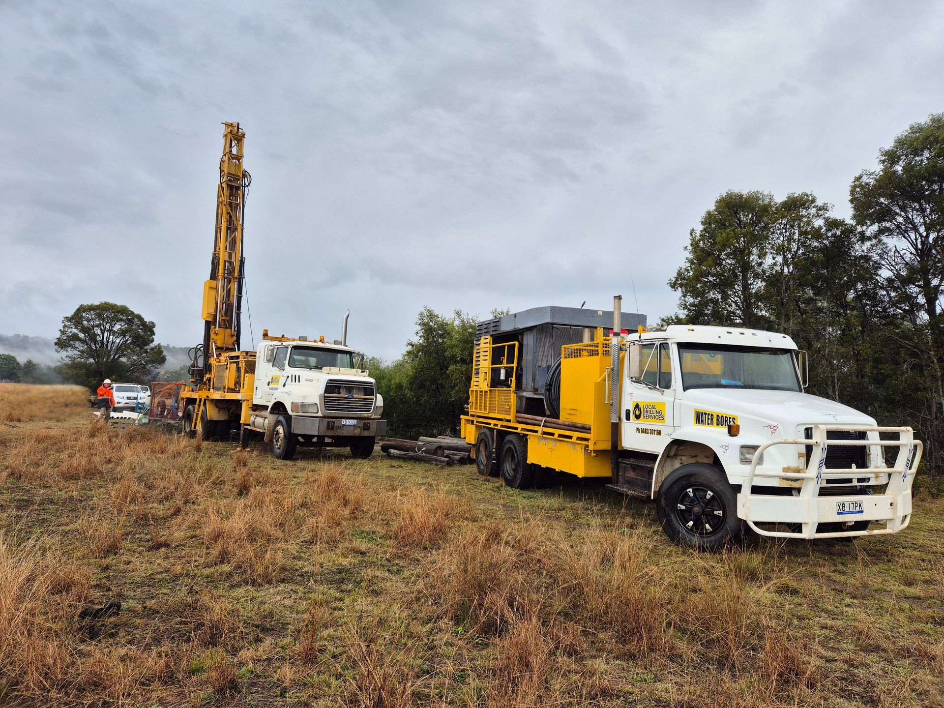 Two Yellow Drilling Trucks in a Field on a Cloudy Day — Local Drilling Services In Yarraman, QLD