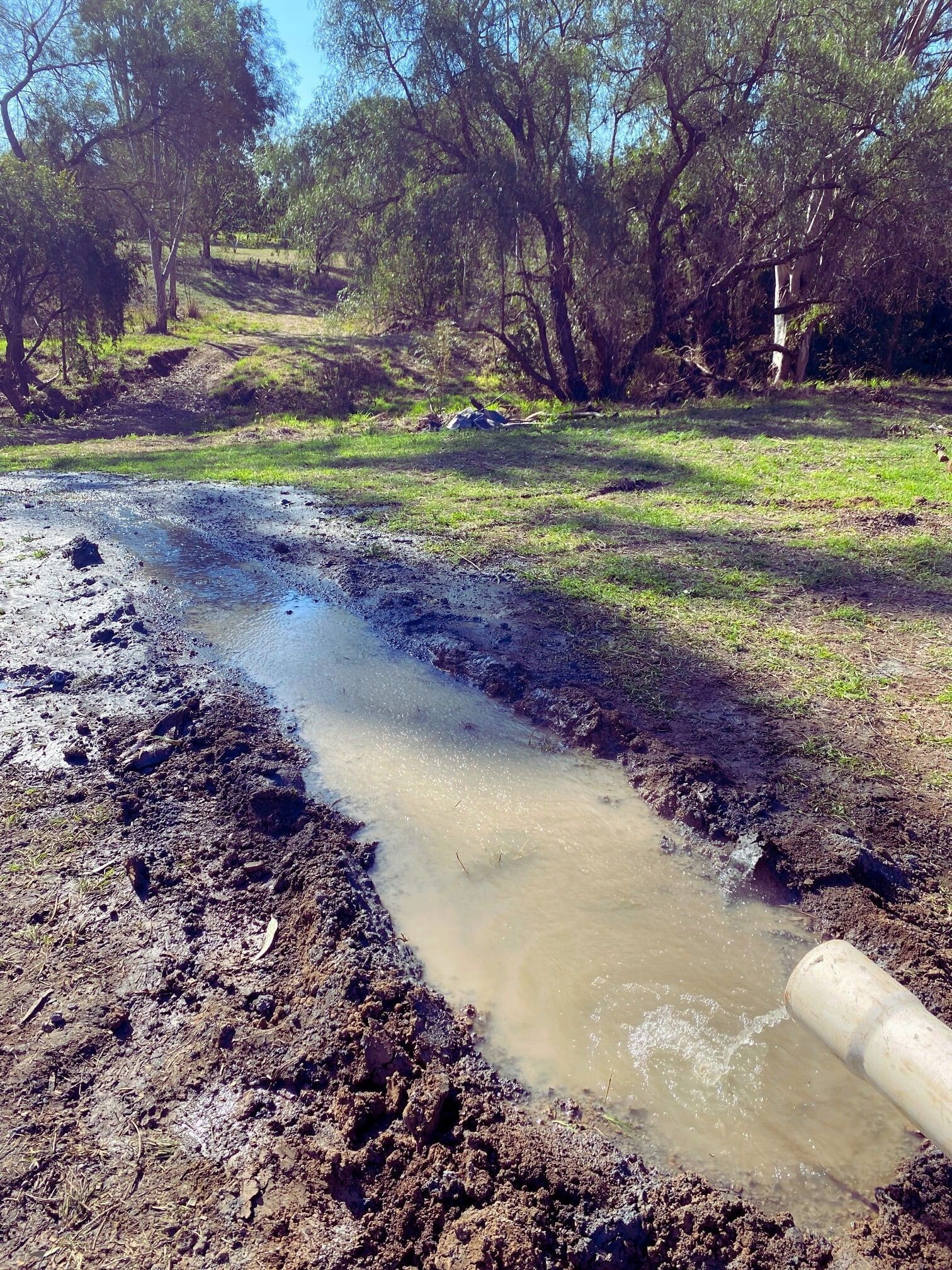 Muddy trench filled with water; a pipe is emptying into the water — Local Drilling Services In Kilcoy, QLD