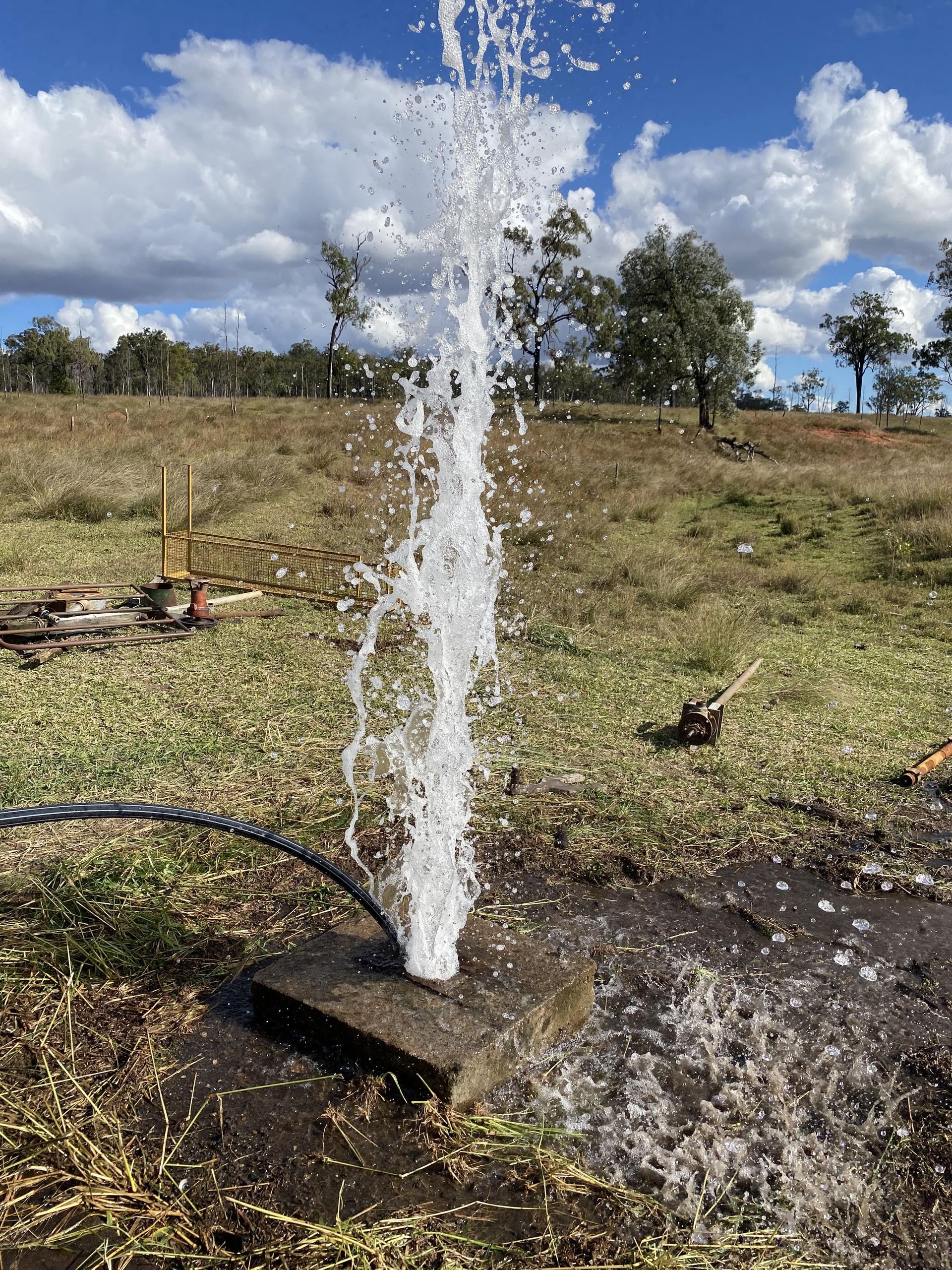 Water gushing from a pipe in a grassy field under a partly cloudy blue sky — Local Drilling Services In Yarraman, QLD
