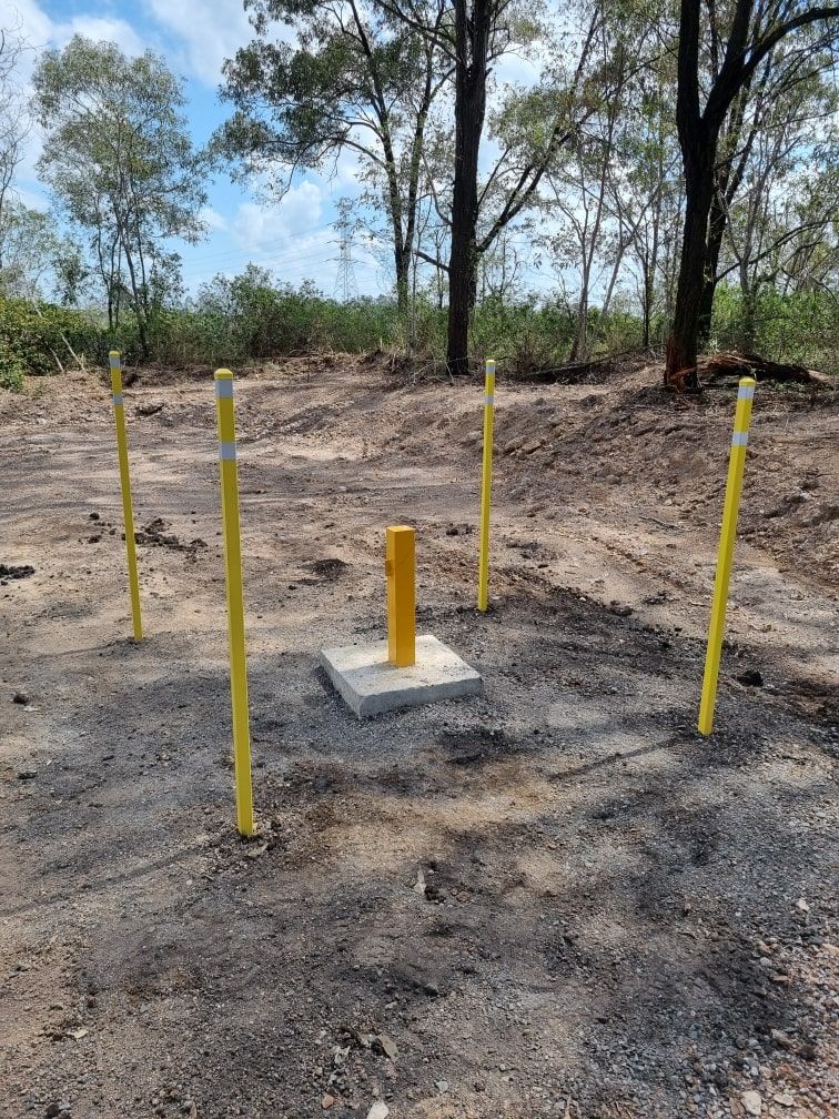 Yellow posts and a yellow pipe on concrete pad in a dirt clearing, with trees in the background — Local Drilling Services In Kingaroy, QLD