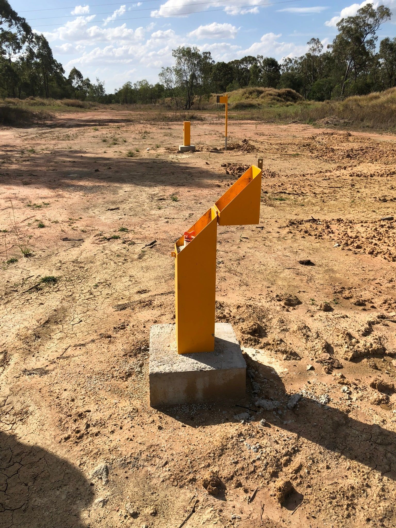 Yellow markers on concrete bases in a dirt field under a cloudy sky — Local Drilling Services In Kingaroy, QLD