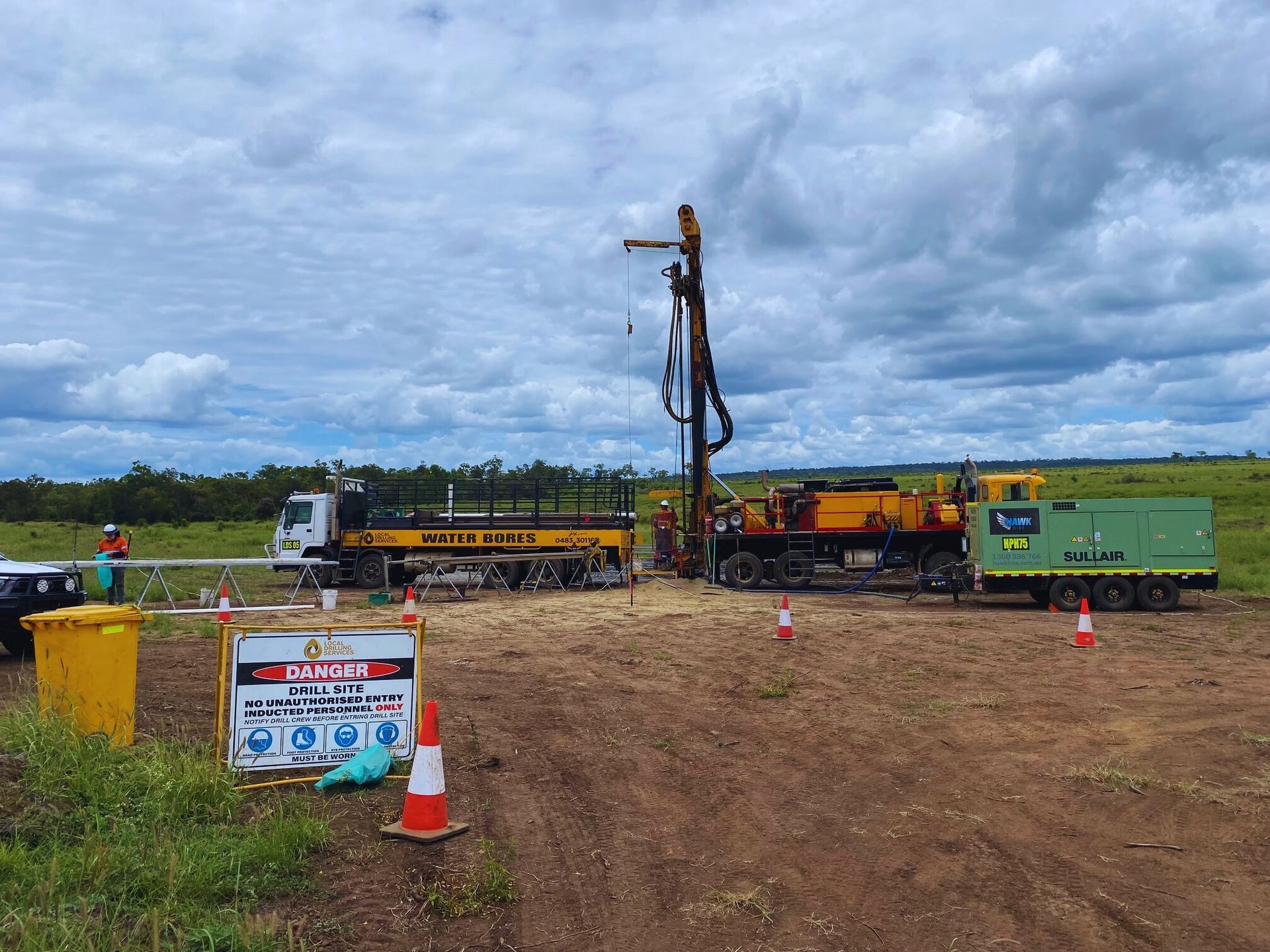 Drilling rig on site, with truck, caution sign, and worker — Local Drilling Services In South Burnett, QLD