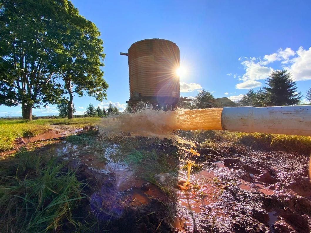 Sun Shining on a Water Tower and Pipe Spewing Muddy Water — Local Drilling Services In Murgon, QLD