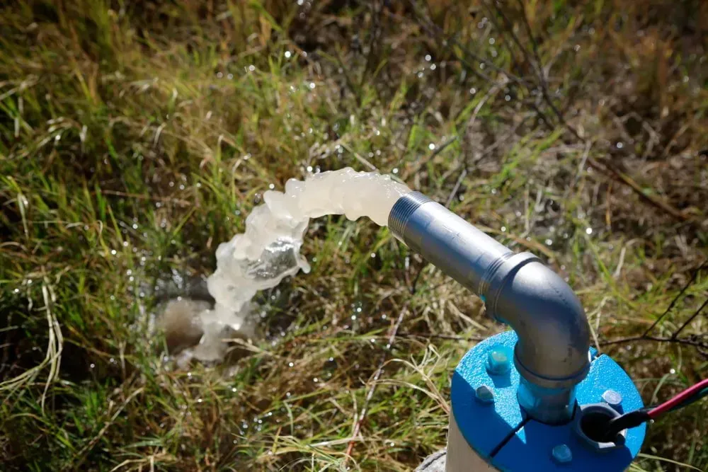 Water Gushing From a Silver Pipe at a Well Head in a Grassy Area — Local Drilling Services In North Burnett, QLD