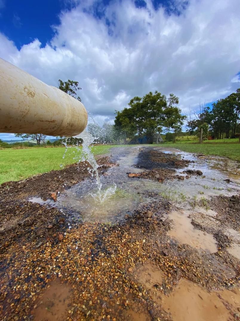Water pouring from a white pipe onto muddy ground — Local Drilling Services In Murgon, QLD