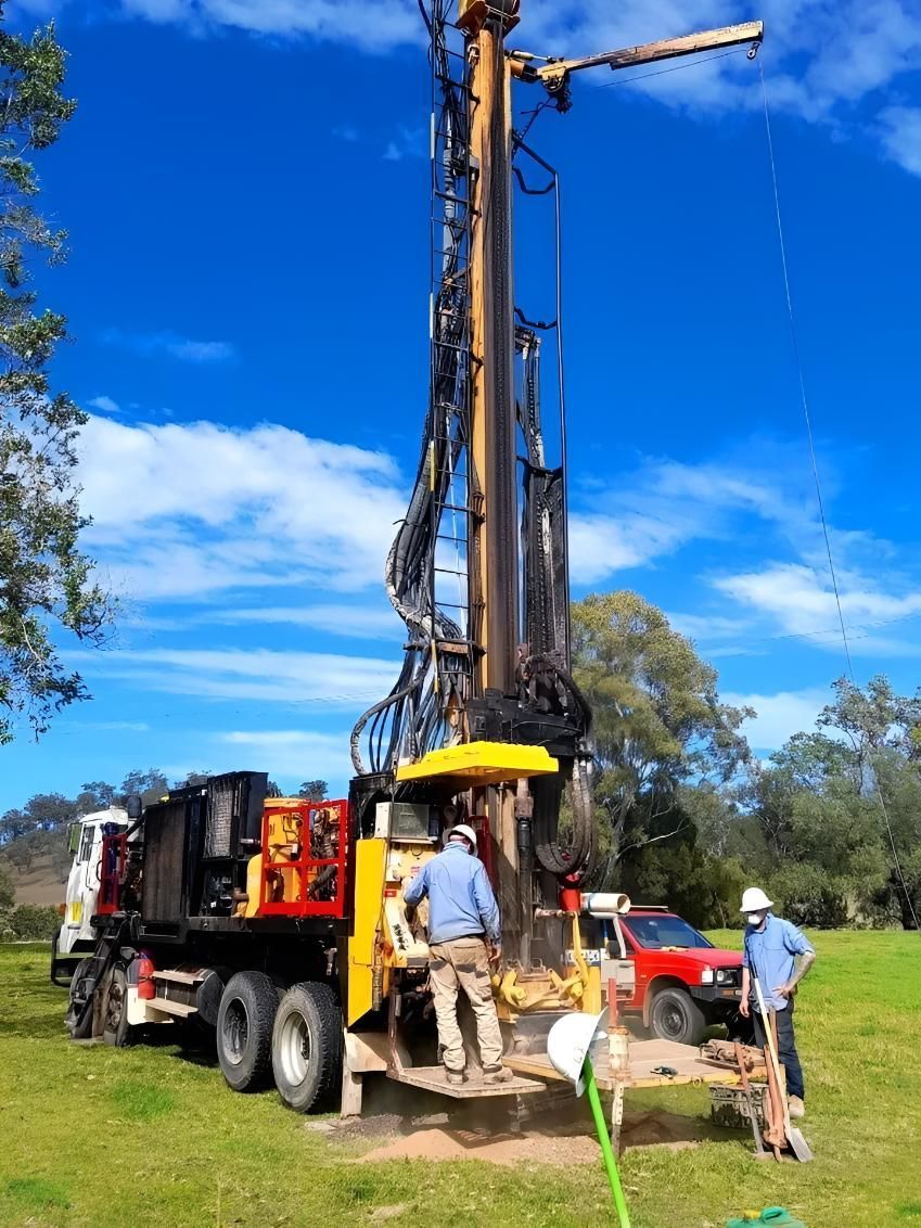 Drilling Rig on a Truck in a Field, Two Workers in Blue Shirts — Local Drilling Services In Kilcoy, QLD