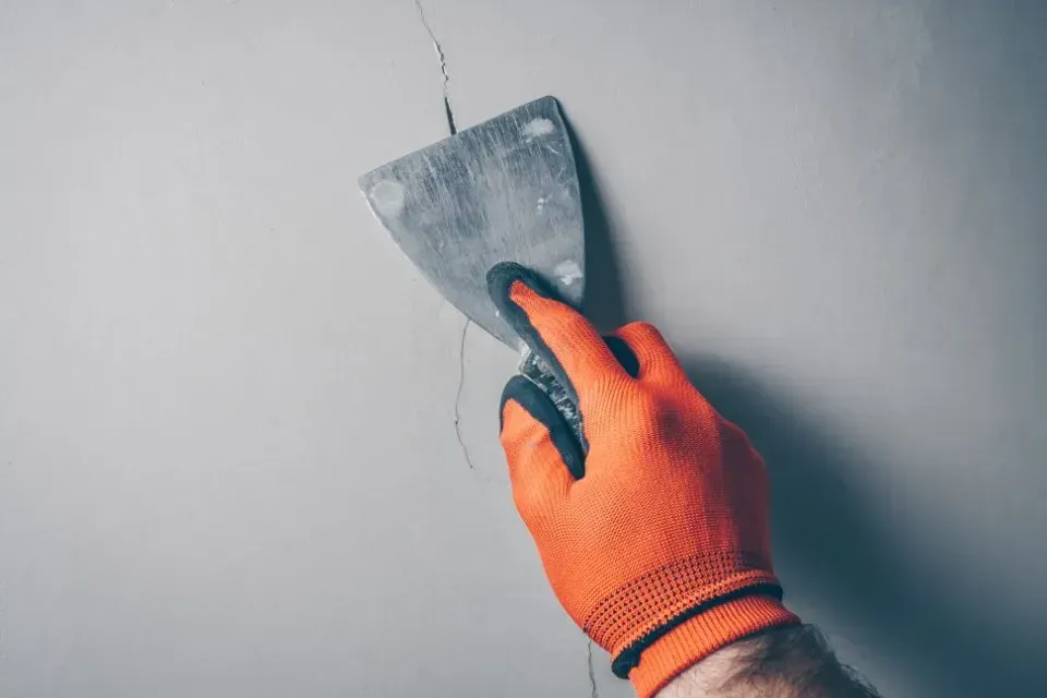 Eine Person hält einen Spachtel in der Hand und verputzt eine Wand.