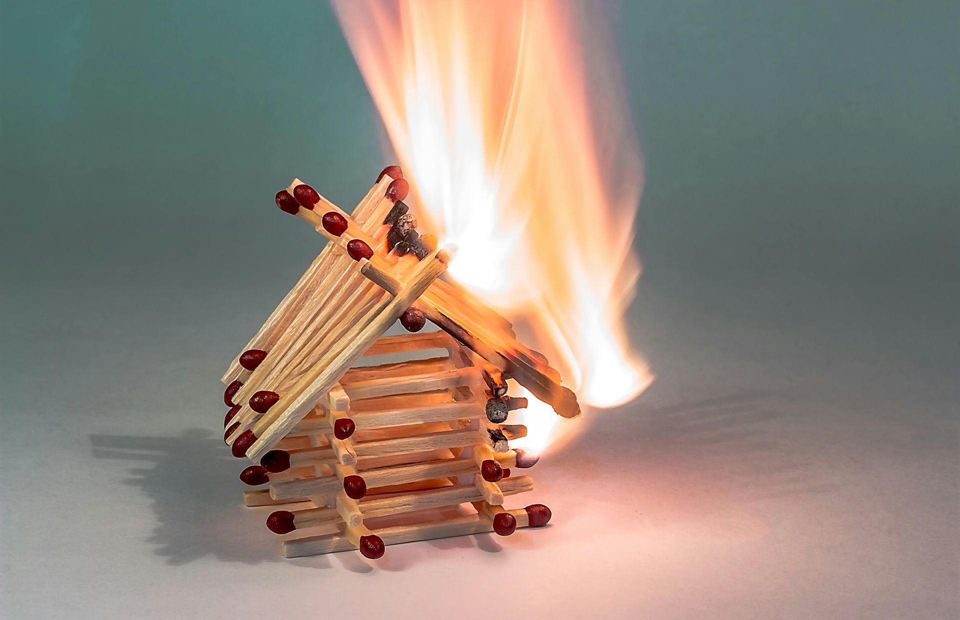 Symbolbild: Brennendes Streichholzhaus – verdeutlicht die Notwendigkeit von baulichem Brandschutz