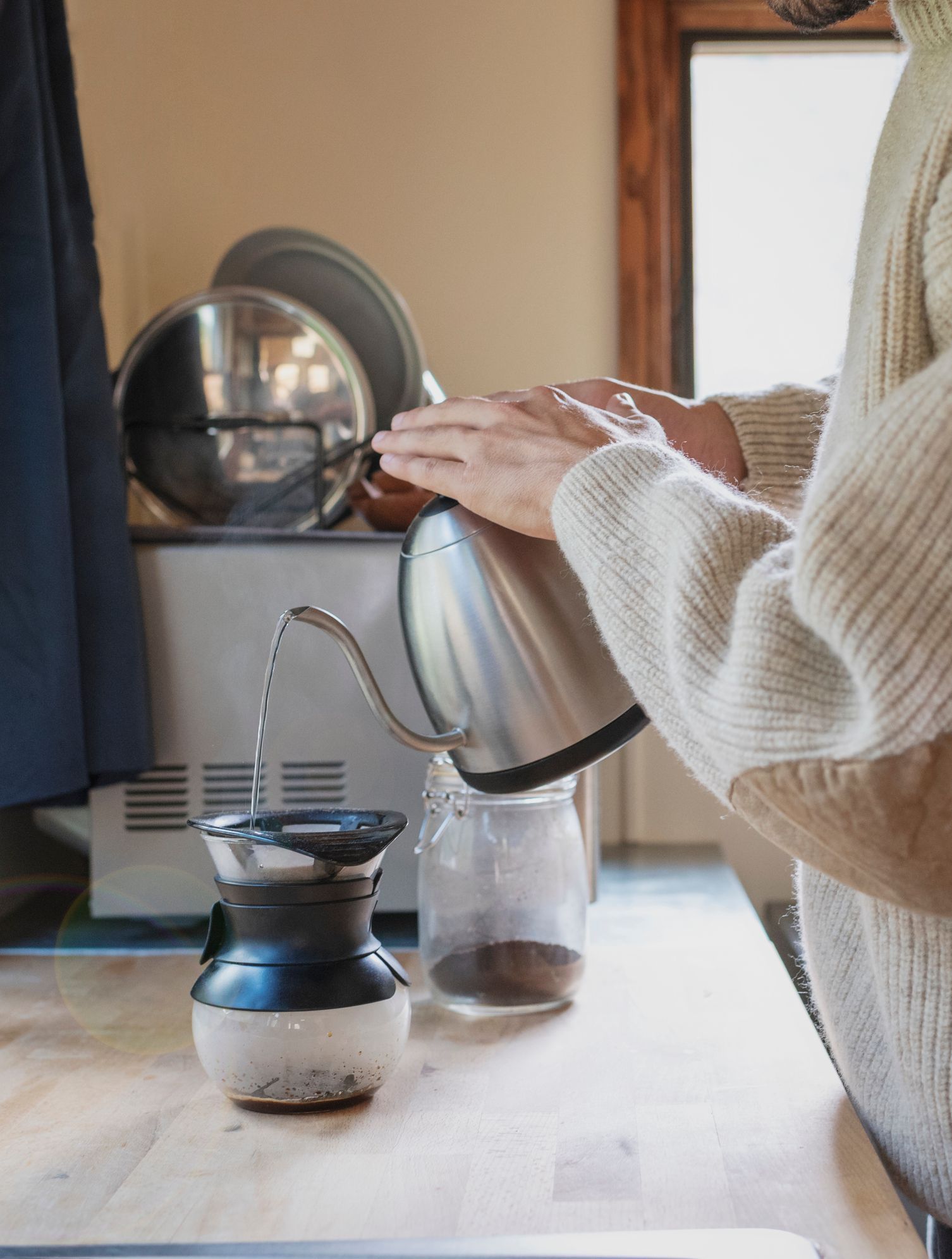 A person is pouring water from a kettle into a glass jar.