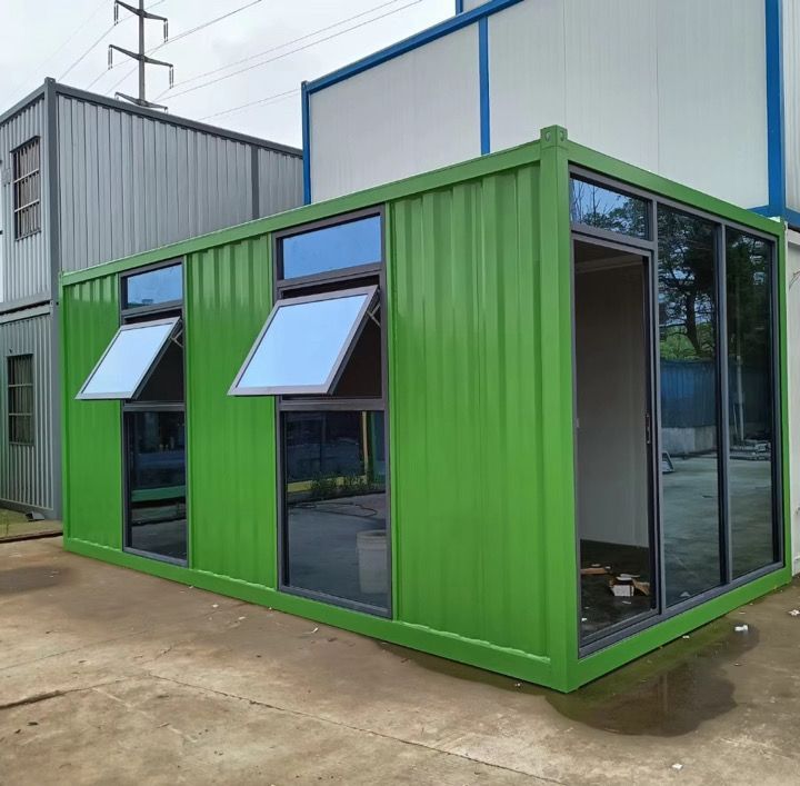 A green shipping container with a lot of windows is sitting next to a building.