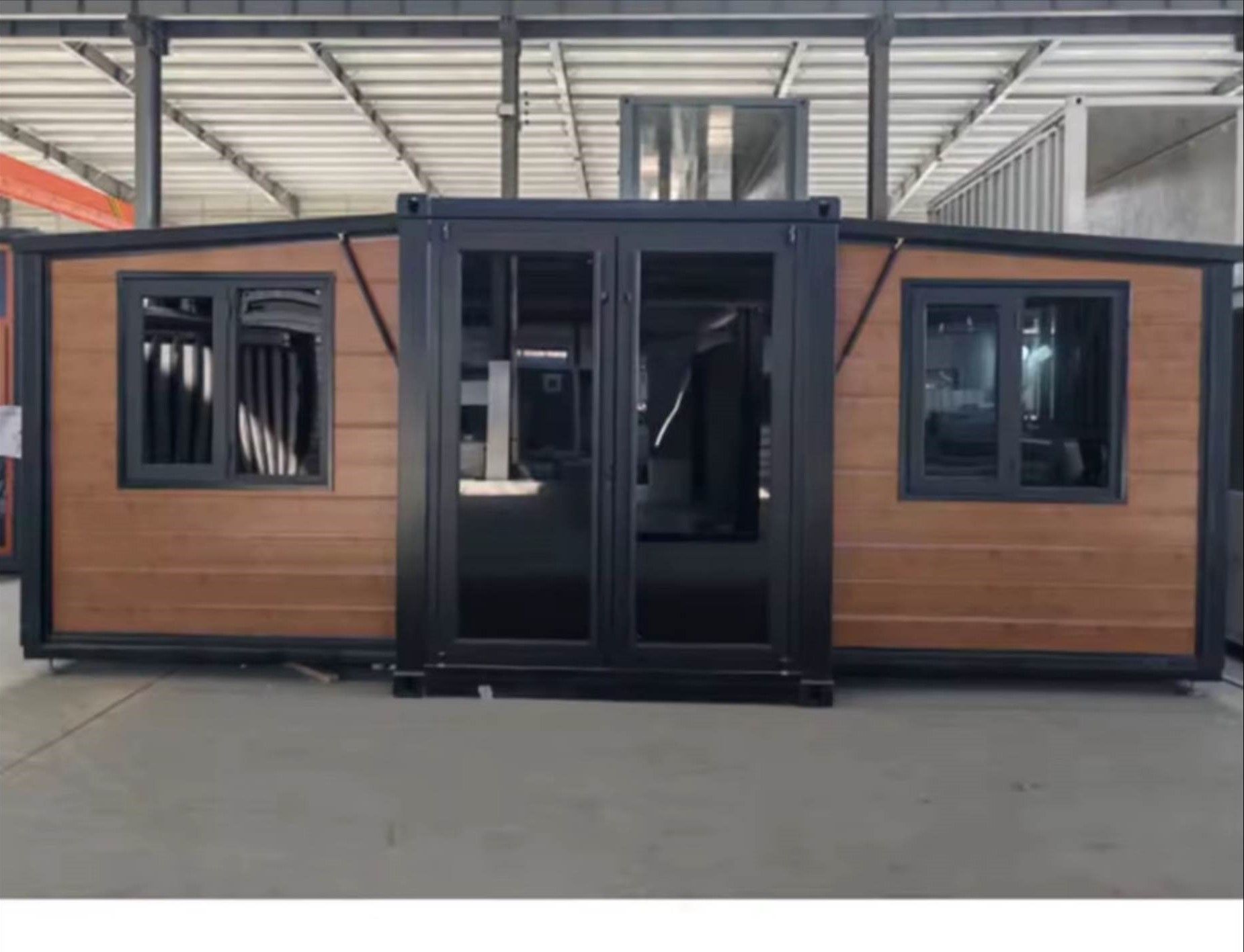 A wooden house with a black door and windows is sitting in a warehouse.