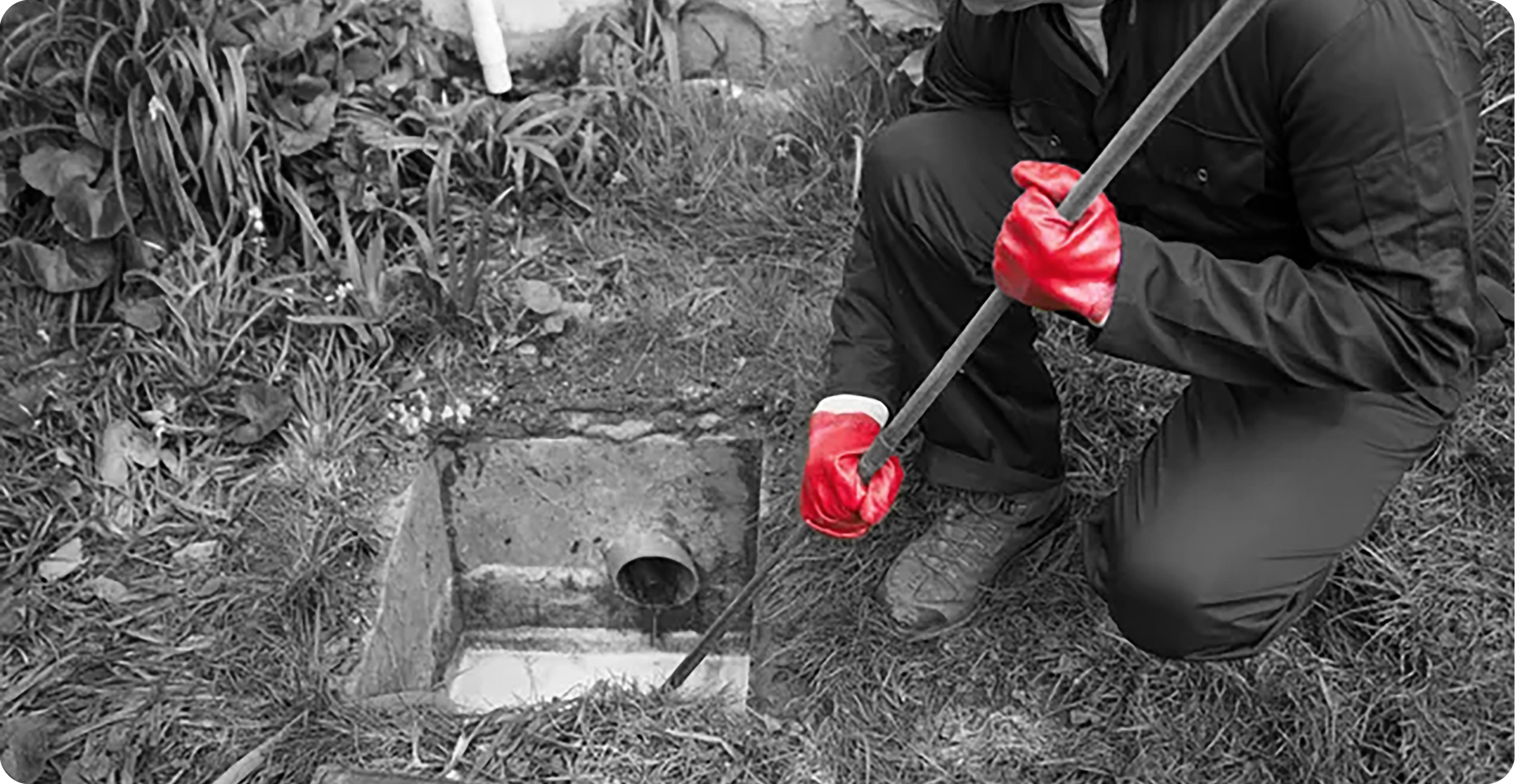 A man wearing red gloves is kneeling down and holding a broom.