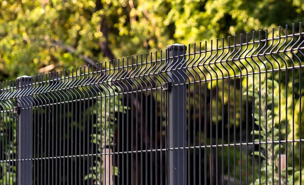 Black metal fence with pointed tops in front of leafy green trees and sunlight