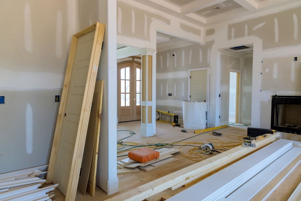 Renovation site with unfinished drywall, lumber, and tools in a bright room and kitchen area