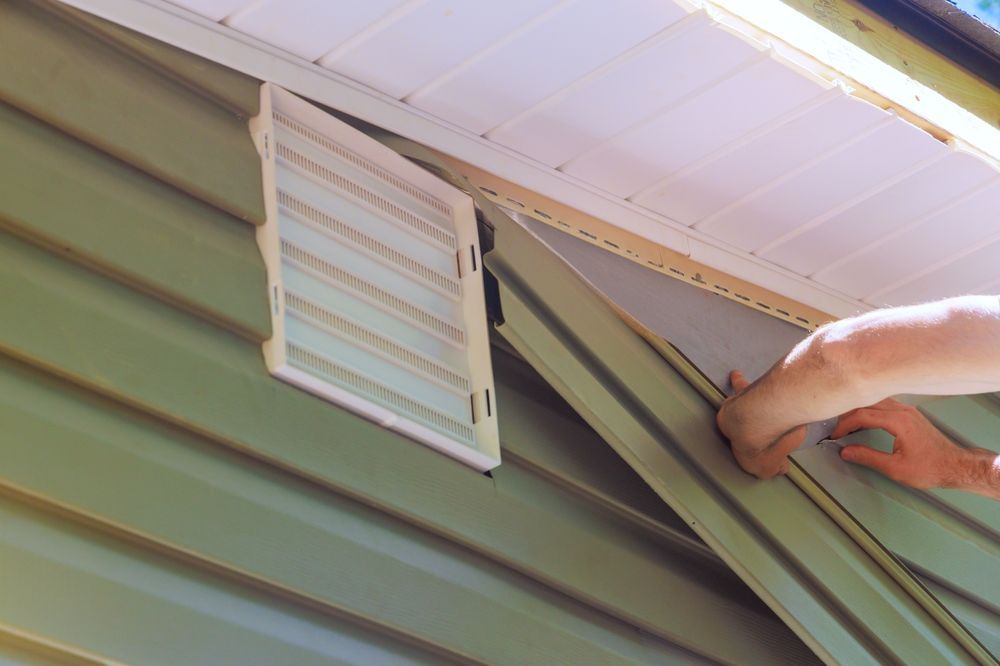 Person installing a vent on a green metal roof near the eaves