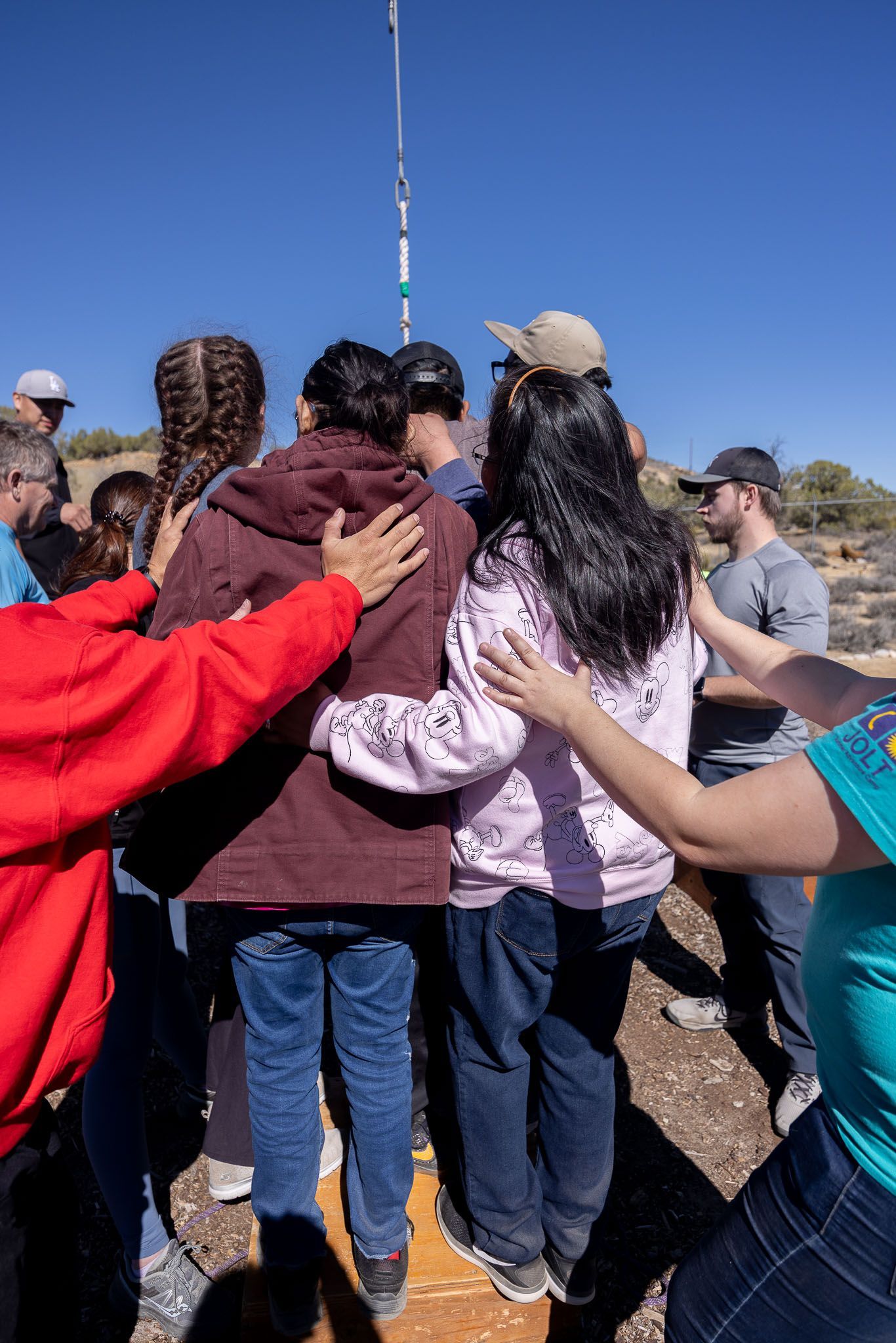 Group of teens in a circle with a person holding a clipboard, discussing in a room.