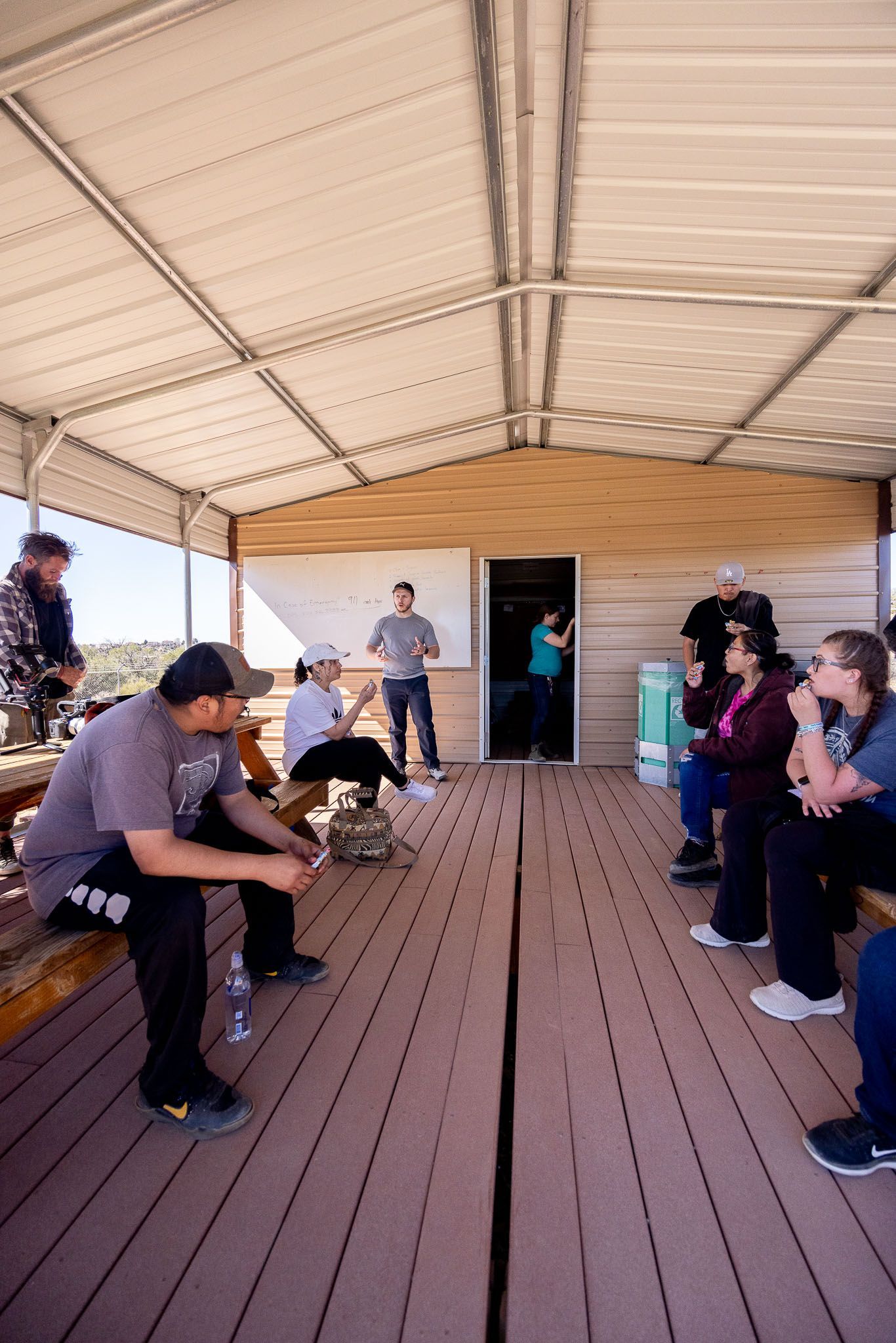 Group of people in casual wear talking and smiling in a well-lit room; some are holding notebooks.