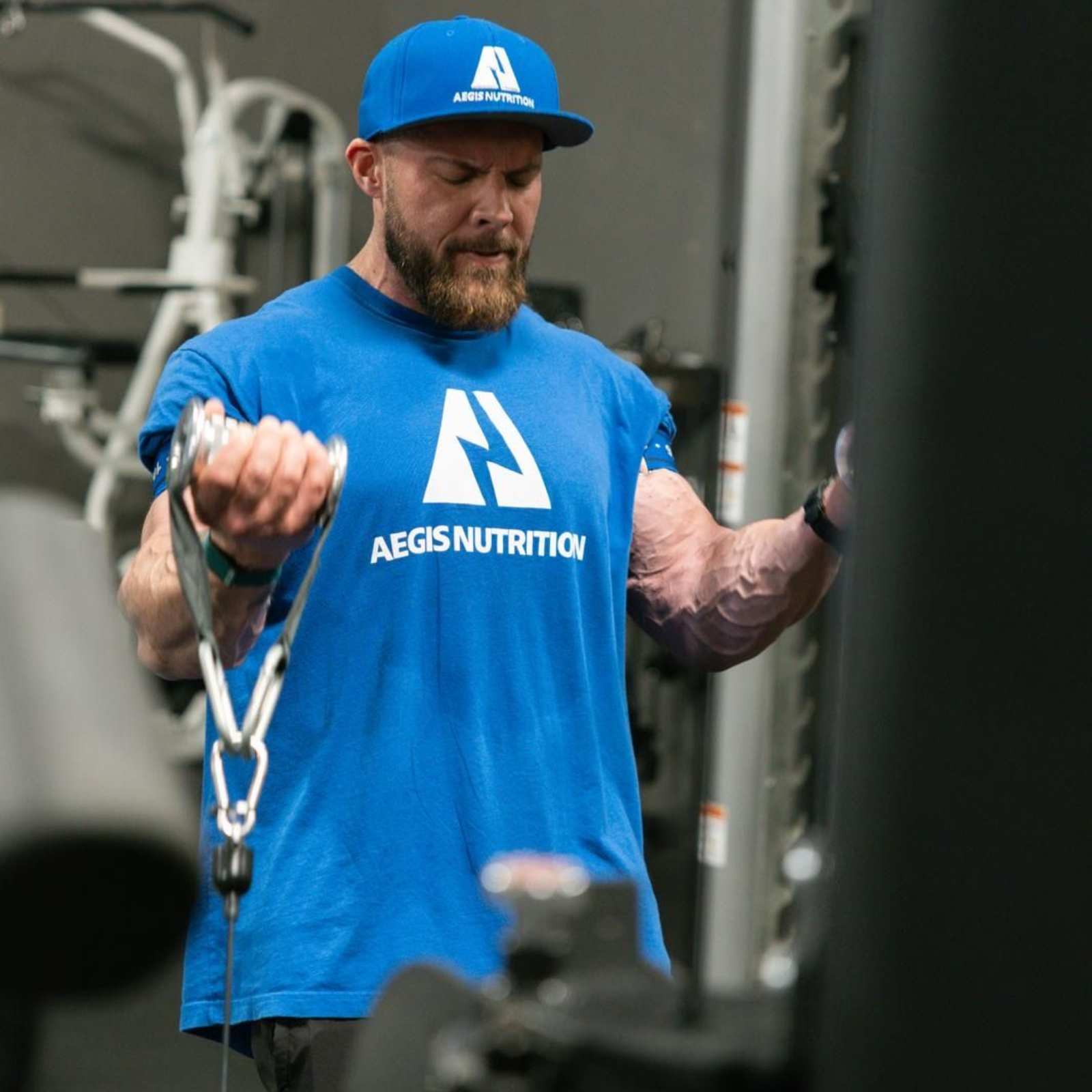 Man in blue shirt and hat doing cable bicep curls at a gym.