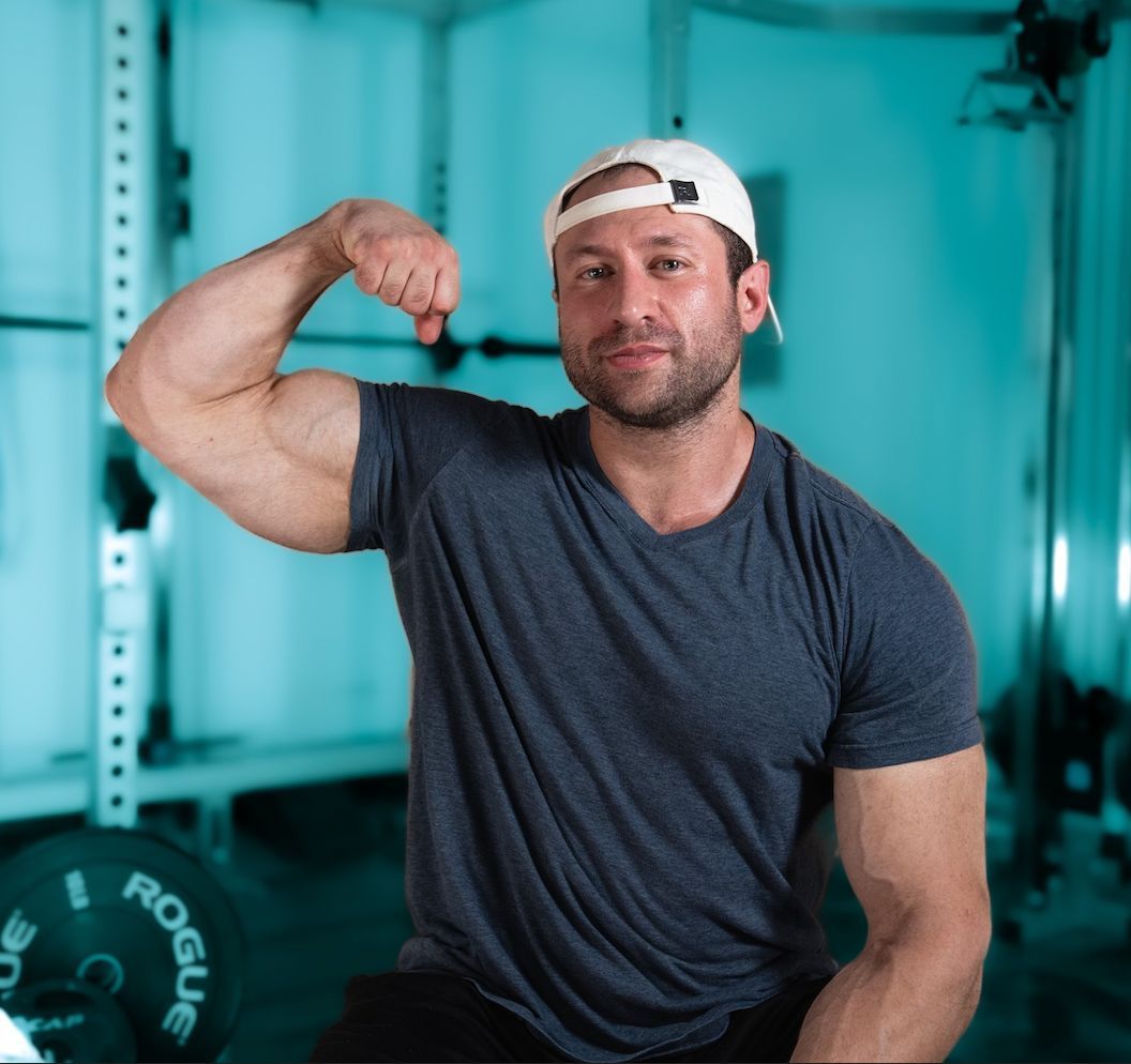 Man in gym, arms raised, celebrating workout. Another man in the background, also in the gym.