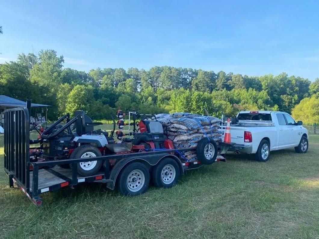 A white truck is towing a trailer with a lawn mower on it.
