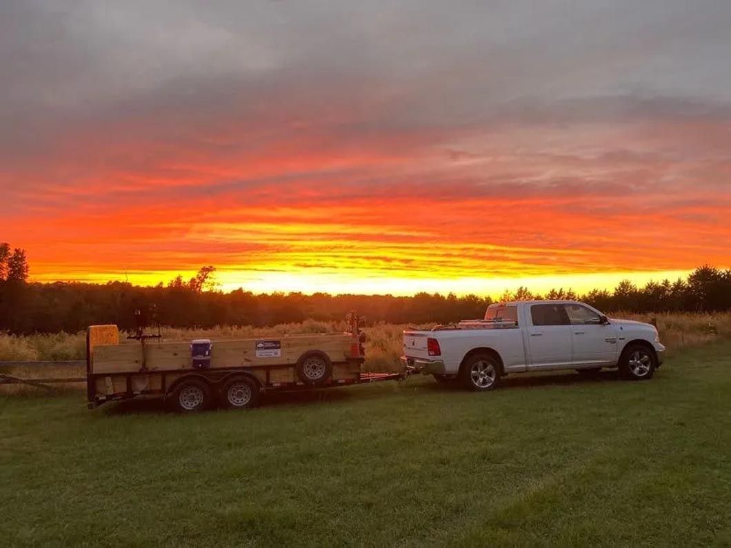 A white truck is towing a trailer in a field at sunset.