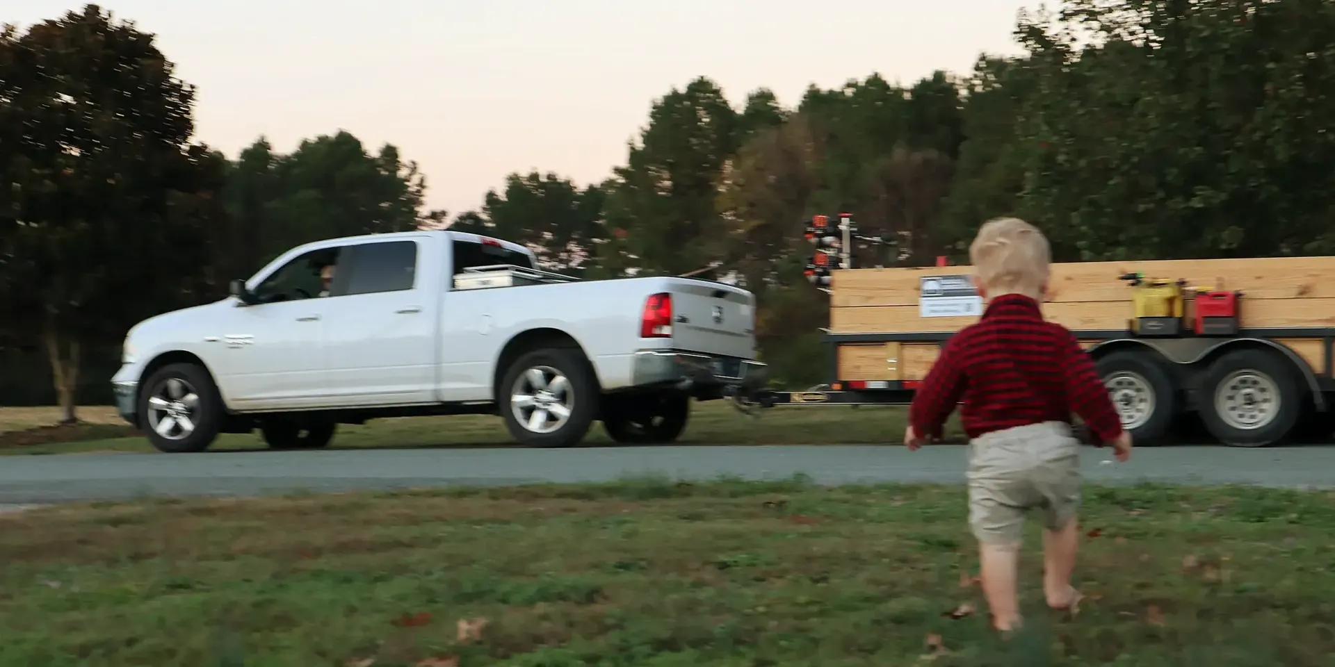 A little boy is running towards a white truck that is pulling a trailer.