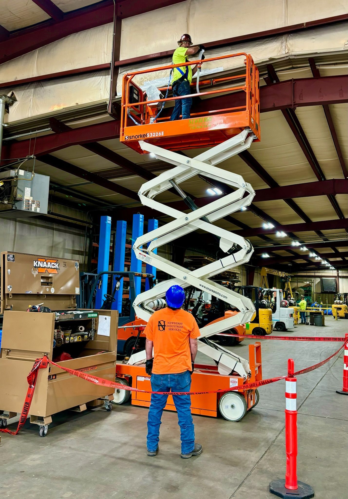 A man is standing on a scissor lift in a warehouse.